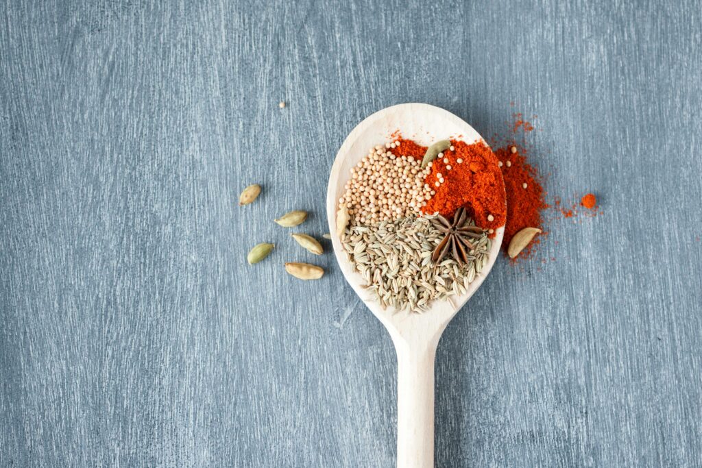 A collection of vibrant spices displayed on a wooden spoon against a textured background.