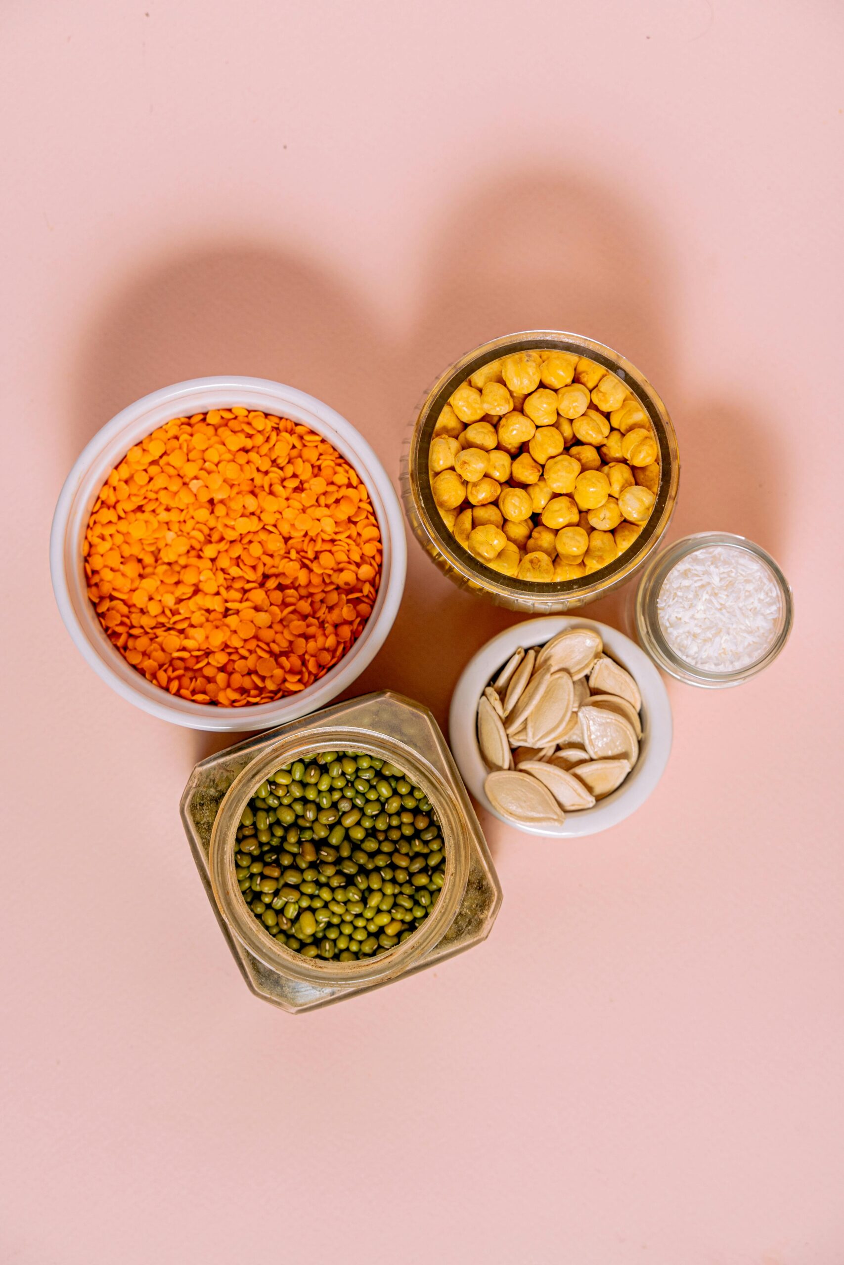 Variety of raw seeds and legumes on pink background for healthy cooking ideas.